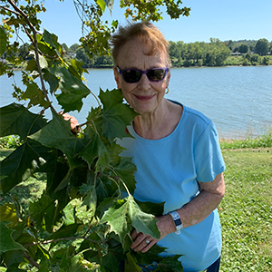 woman in blue shirt smiles by body of water and trees