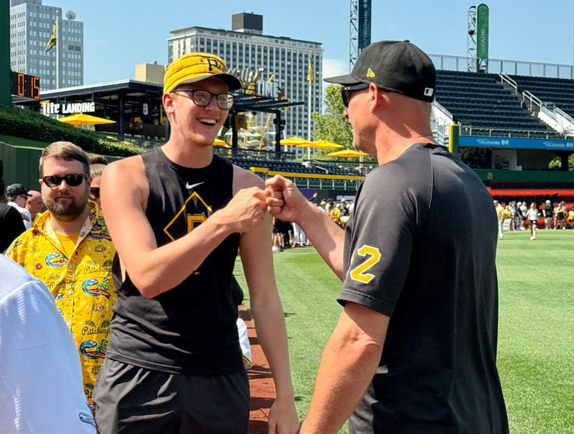 A man wearing a yellow pirates hat smiling, bumping fists with another man wearing a black pirates baseball hat and shirt.
