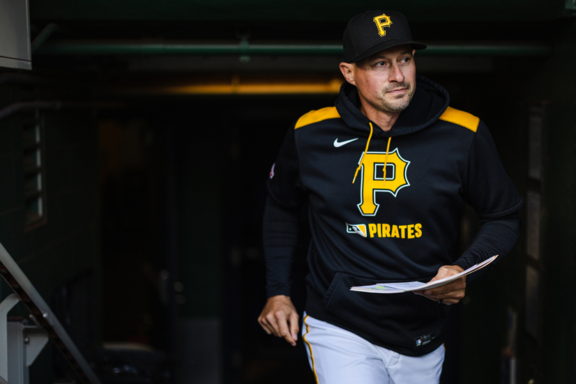 A man wearing a pirates hat and hoodie holding papers, in front of a dark background