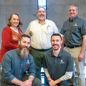 Four men and one woman posing for a group picture smiling.