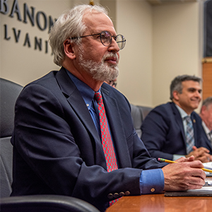 manw ith beard and glasses looking in distance at commission meeting