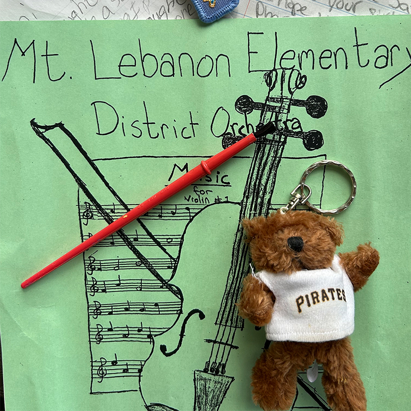 green paper with child's writing and music sheet, paintbrush and teddy bear with Pirates baseball jersey