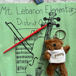 green paper with child's writing and music sheet, paintbrush and teddy bear with Pirates baseball jersey