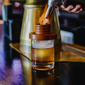 A smoked peach old fashioned being smoked by a fire