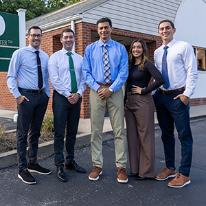group photo of four men and one woman wearing business clothes outside of a business