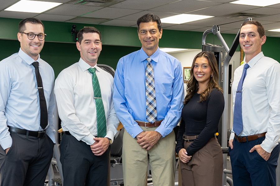 group photo of four men and one woman in a gym wearing business clothes