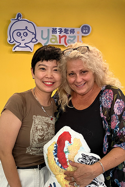 two women smiling, one holding a pillow, in a room with yellow walls