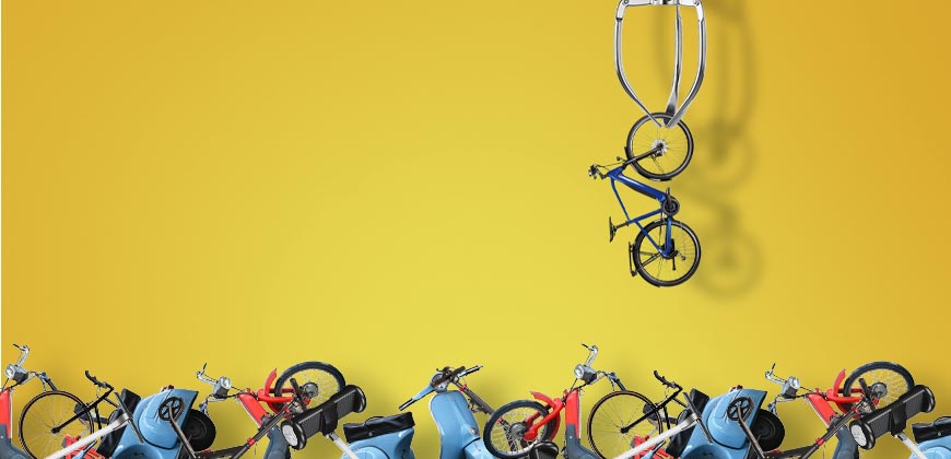 a depiction of a crane game, a crane picking up a bike out of a bunch of different types of bikes piled at the bottom