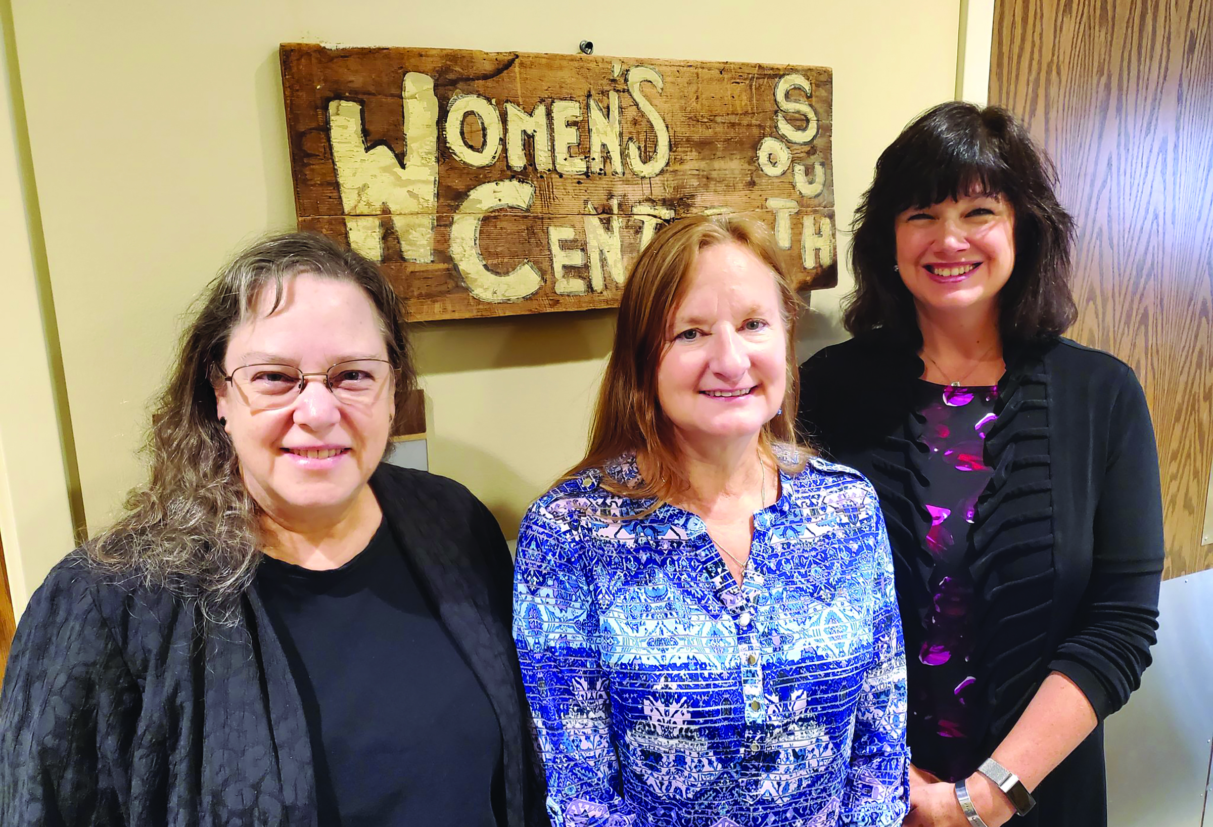 a portrait of 3 women, one with glasses and brown hair, one with red hair and one with black hair, in front of a sign that says "Womens Center South"