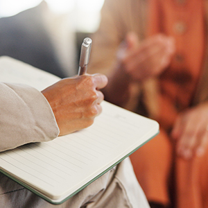 person writing in notebook and blurry person in background