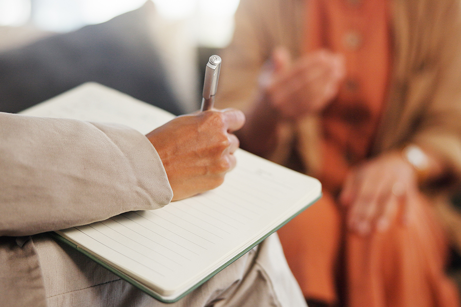 person writing in notebook and blurry person in background
