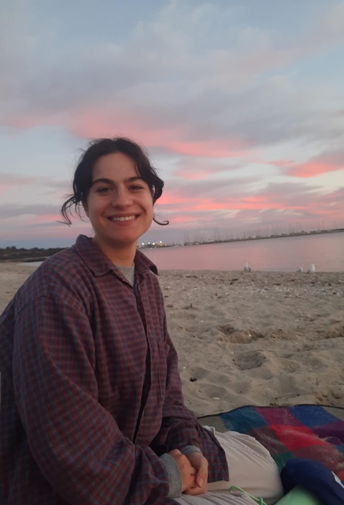 young woman smiling sitting on beach at sunset