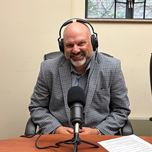 man in grey suit with headphones and microphone smiling