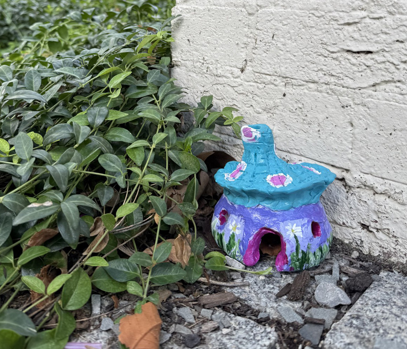 a small sculpture that looks like a house made out of a mushroom painted with blues and purples sitting next to some plants
