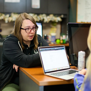 woman with glasses talking to someone off camera with a laptop