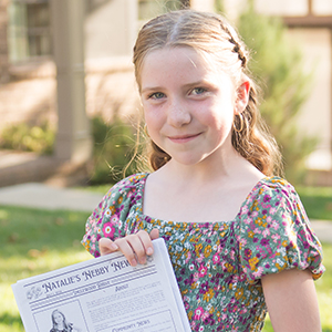 girl with blonde hair holding newspaper smiling
