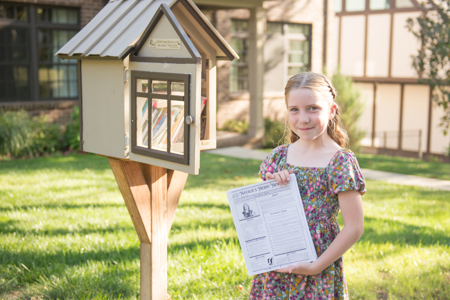girl in dress holding newspaper by a little library