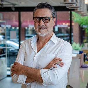 man with glasses and white shirt with arms folded in a storefront