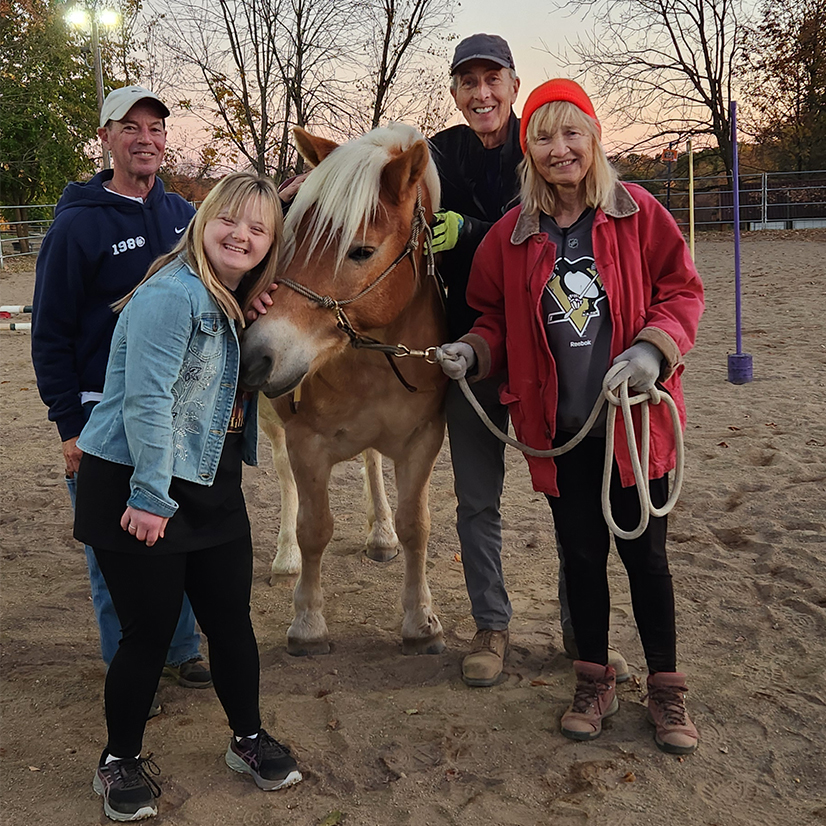 four people smiling with a horse outdoors