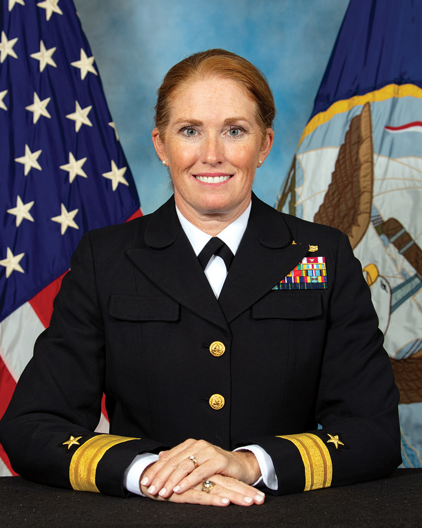 woman in navy uniform smiling in front of flags