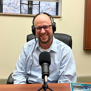 Man with glasses on wearing headphones in front of a microphone