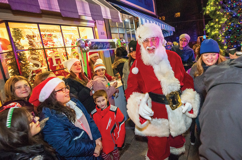 santa clause dressed in red and white with a beard, leaning in for a handshake surrounded by peopl eon the street, a christmas tree in the background