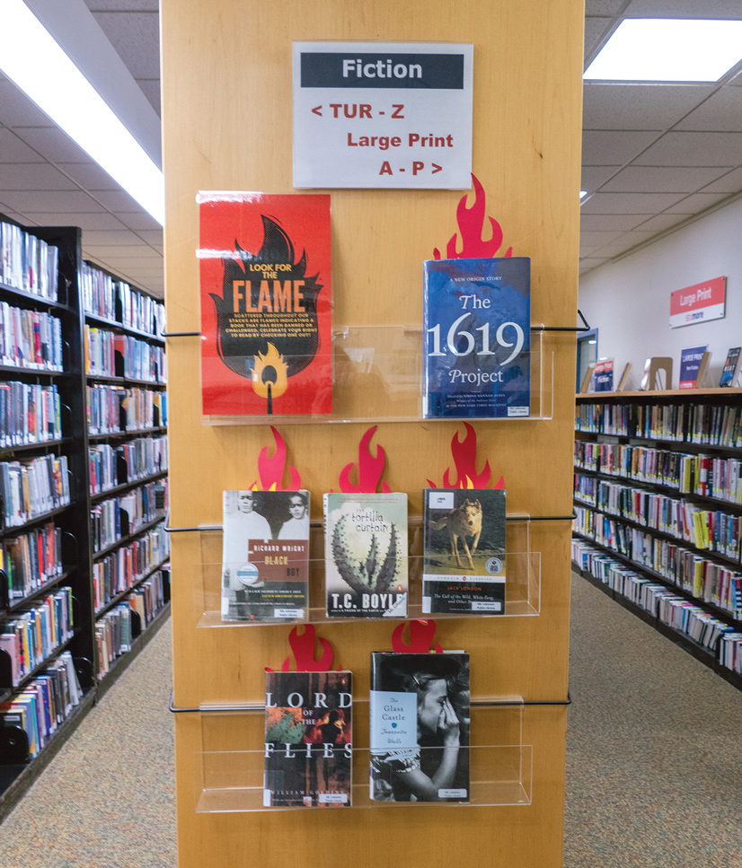 banned books displayed in a library with flame book marks coming out of the top of them.