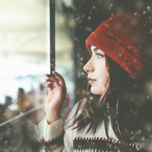 Side view of woman wearing a red beanie hat and white sweater looking through window.
