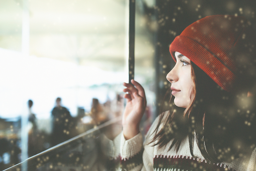 Side view of woman wearing a red beanie hat and white sweater looking through window.