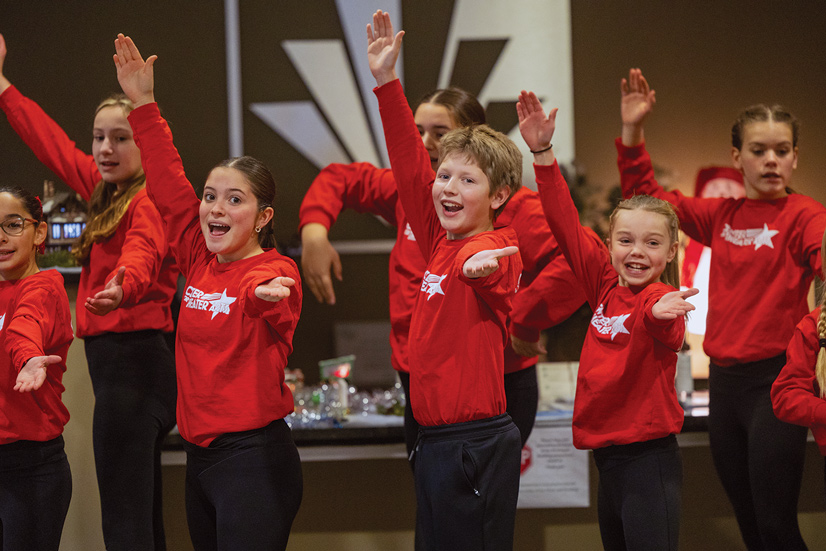 many adolescent age kids wearing red sweatshirts dancing in unison in the municipal building