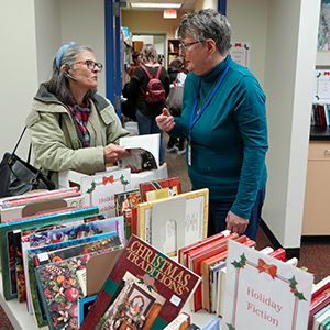 two women talking near a table with books in the library