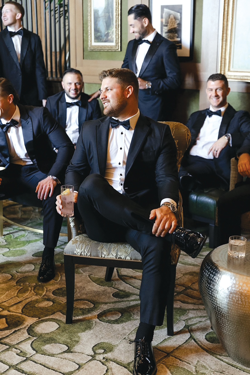 Several men in black bow ties, black tux suits and white shirts lounging, drinking and smiling