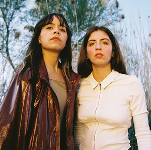 two women with dark hair standing in front of some trees