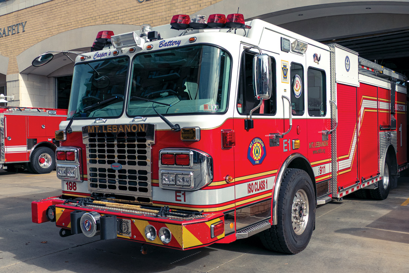 an older red and white pump fire truck parked in front of the public safety building.