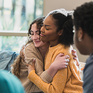 Two young women hugging during emotional support group session.