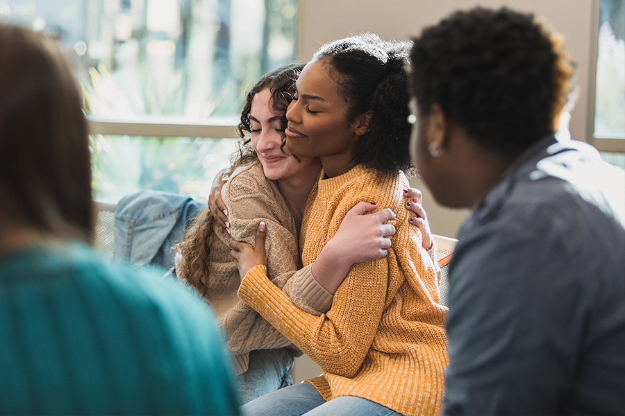 Two young women hugging during emotional support group session.