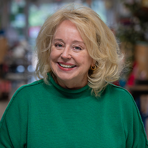 A women with short blonde hair wearing a bright green sweater smiles at the camera.