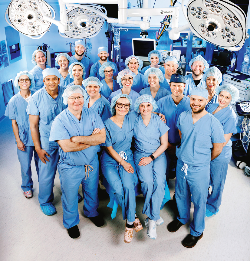 many people standing in a surgery room wearing blue scrubs, and hairnets