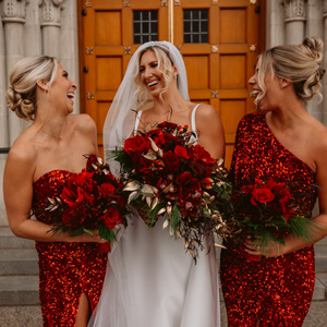 bride and two bridesmaids in red gowns smiling outside church