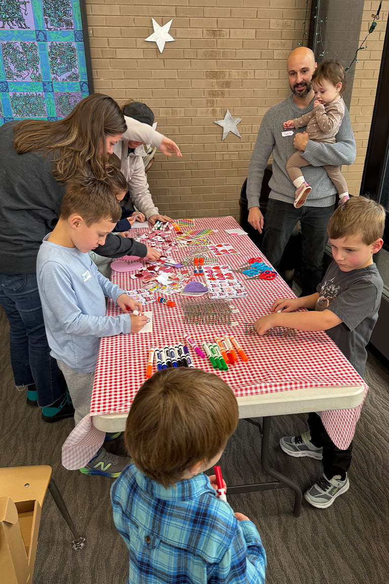 Parents and children gather around a table to make Valentine’s