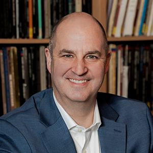 An environmental headshot of a man wearing a navy blue blazer and a white button down shirt.