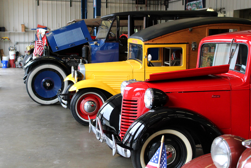 a row of classic cars from the 30s and 40s that are blue yellow and red, parked in a garage