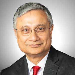 A professional headshot of a man with short gray hair and glasses wearing a black blazer, red tie and white button down shirt.