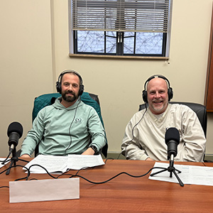Two men sitting with headphones on in front of microphones.