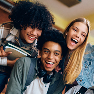 Group of cheerful high school students taking selfie with cell phone in hallway.
