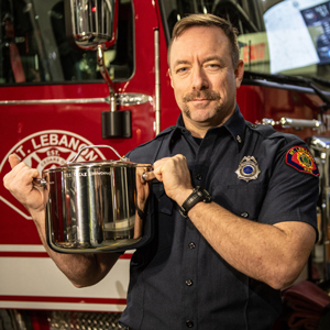 firefighter holding a chili pot in front of a fire truck