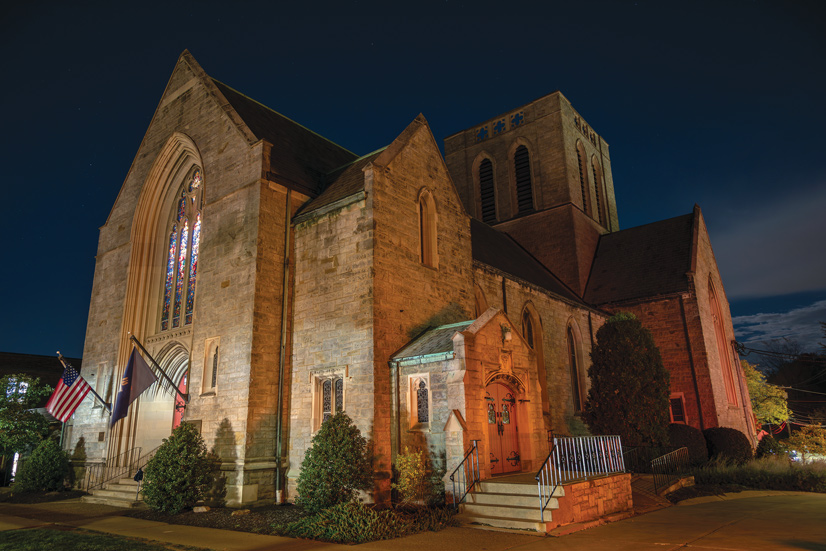 The outside of Southminster Presbyterian church, a large brick buidling with lare stained glass windows, flags fly at the entrance, and there are some decorative shrubs around