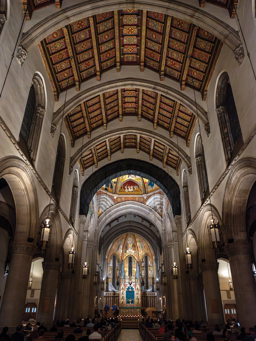 the inside of St. bernards catholic church large ceilings lined with gothic architecture and a massive orgon in the back with gold statues and figues, and religious paintings