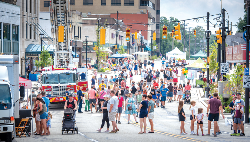 A crowded main street lined with booths and activities for people. There is also a firetruck parked on the side of the road.
