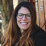 headshot of woman smiling with glasses and long brown hair